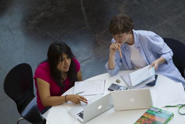 Students reviewing papers on table with laptops
